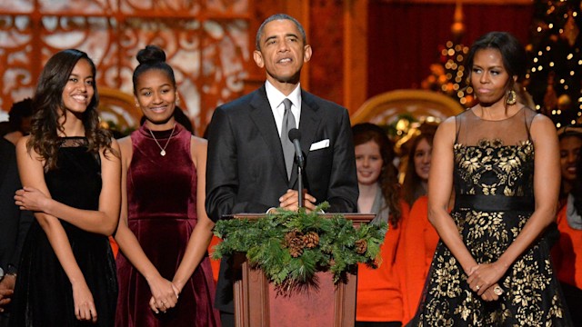 Barack Obama talking to a crowd with Michelle by his side and his daughters