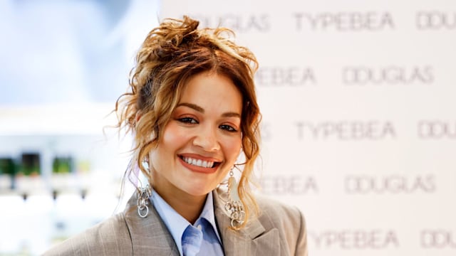 British singer and actress Rita Ora during the Douglas x Typebea Beauty Launch Event on April 1 wearing a grey blazer, blue shirt and long silver earrings