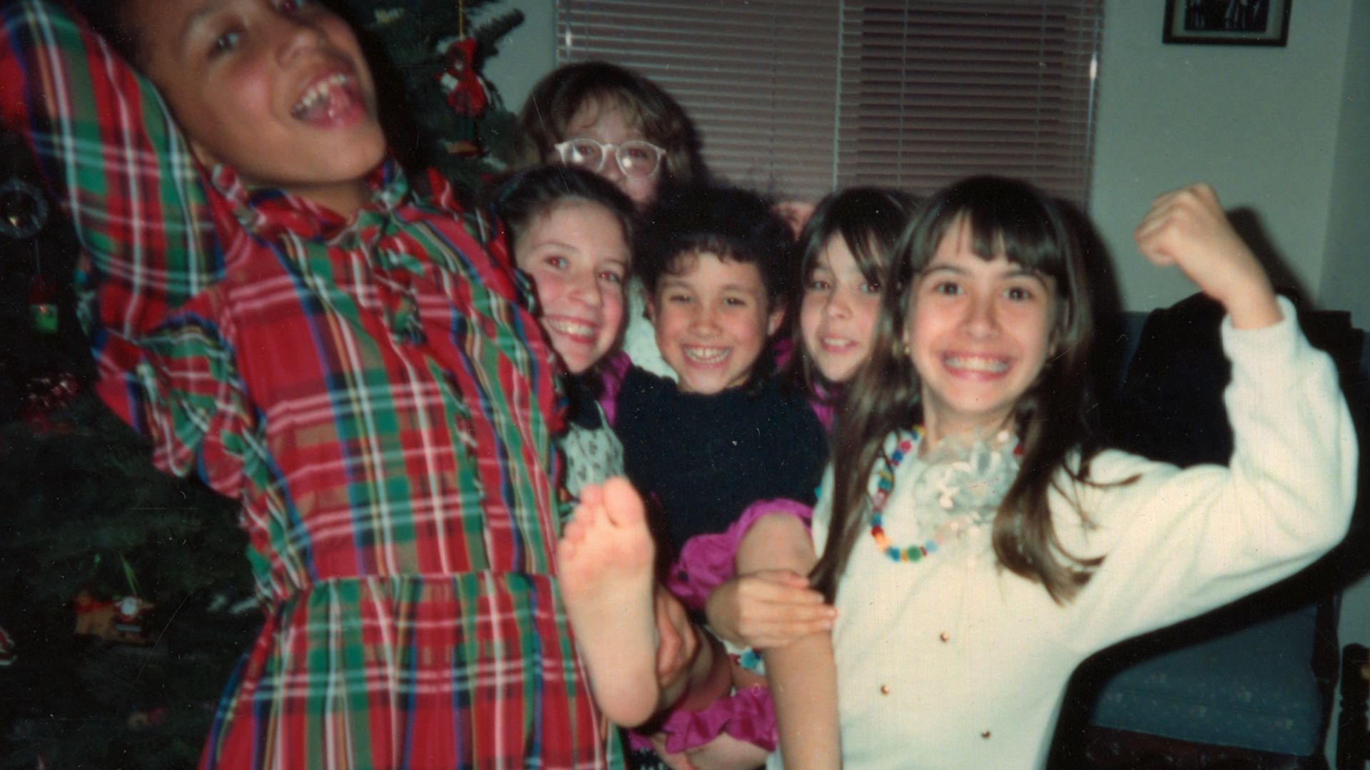 A young Meghan Markle being picked up by a group of friends with a Christmas tree in the background
