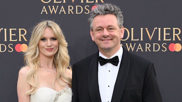 Anna Lundberg in a white dress hodling hands with Michael Sheen who wears a black tuxedo