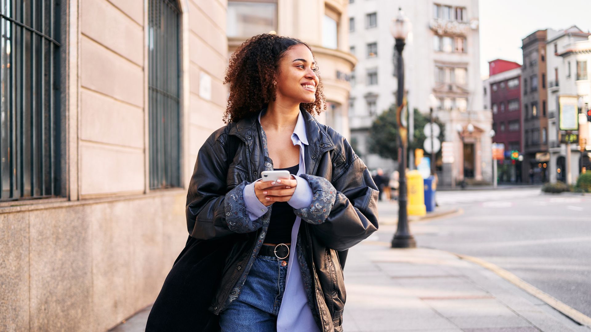  a smiley woman using a mobile walking in the street