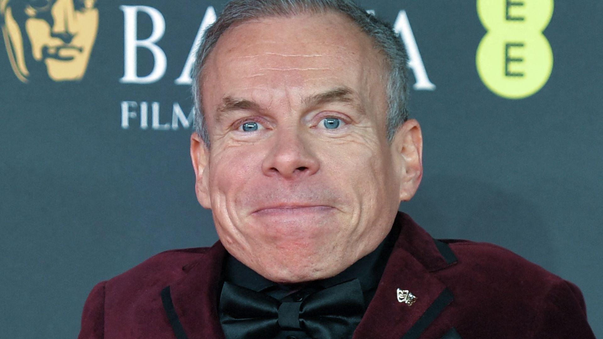 Warwick Davis in a red suit at the BAFTAs