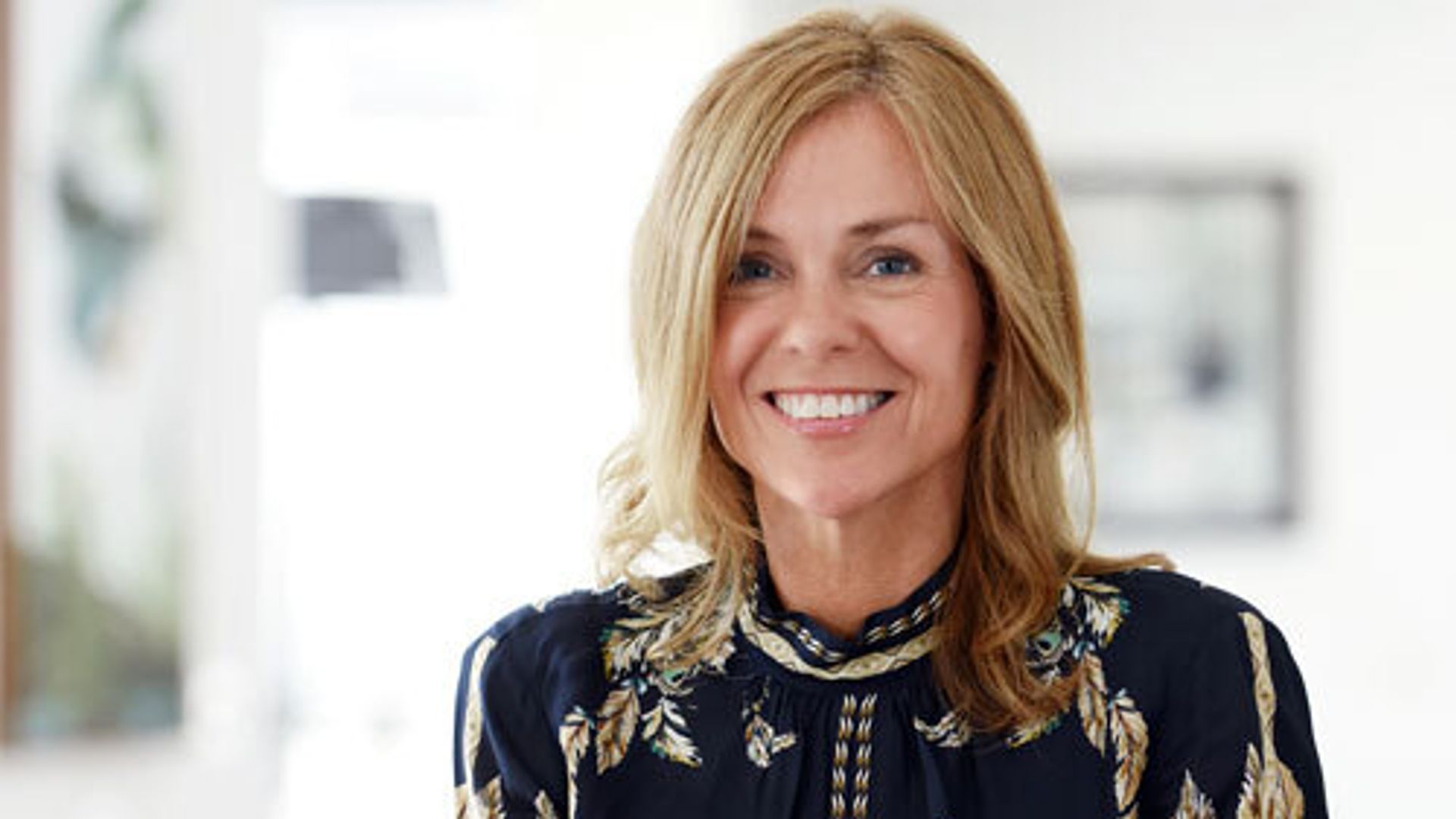 pretty woman in a printed top smiling while holding a mug