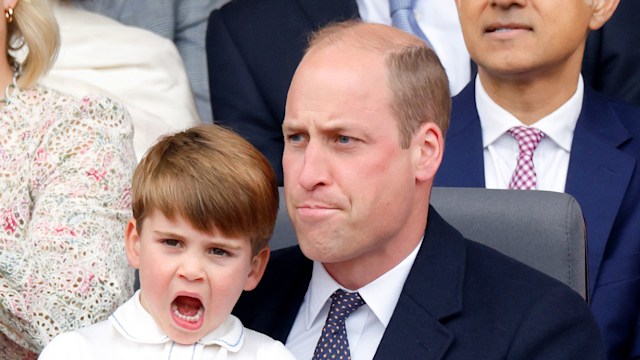 Prince Louis yawning on the lap of Prince William who is pursing his lips