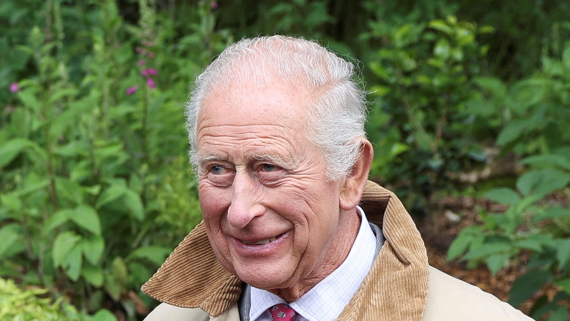 king charles in coat posing with plaque in woodland area