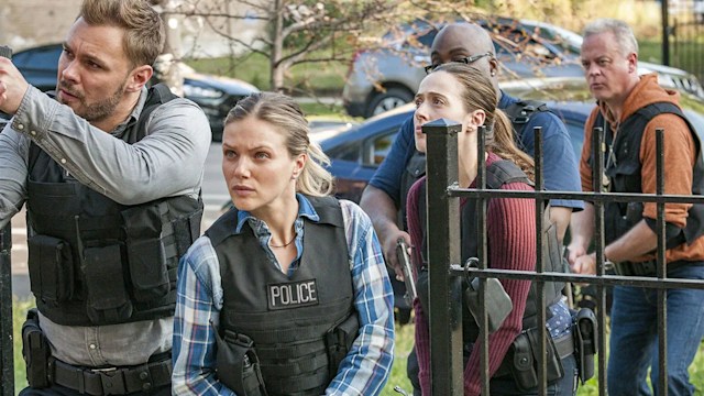 Still from NBC's Chicago PD; Patrick John Fleuger, Tracy Spiradakos, and Marina Squerciati stand in the gate of a home