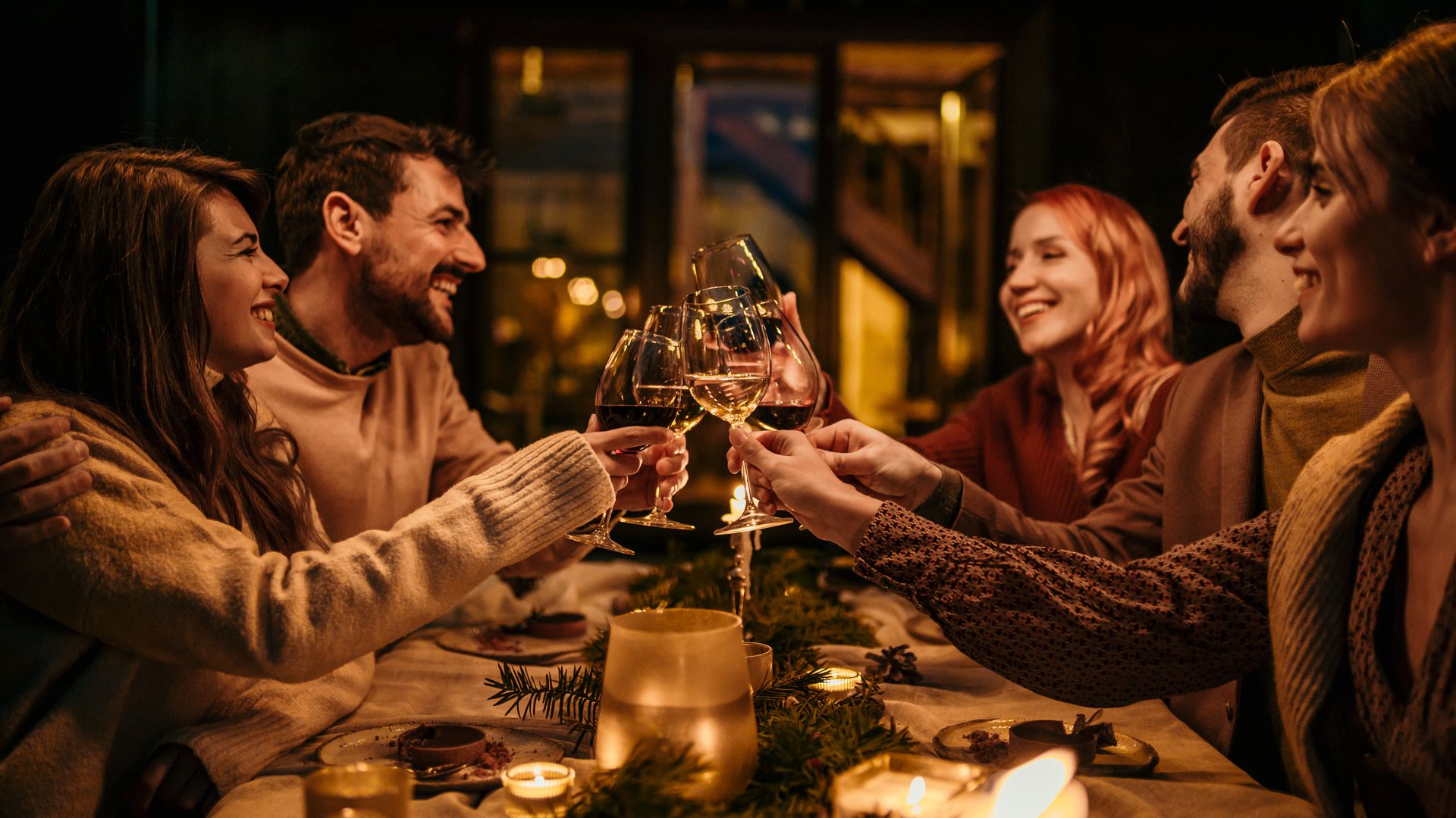 Group of elegantly dressed friends having a small boho dinner/wedding outdoors in a garden, drinking wine, and talking to each other with a great mood and smiles.