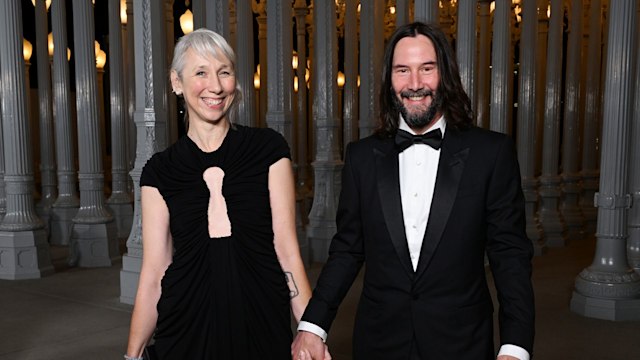 Alexandra Grant and Keanu Reeves smiling and holding hands in black outfits