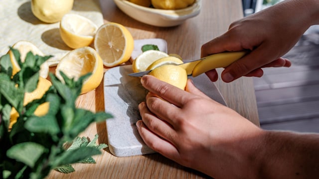 Side view of hands cutting slices of lemon on a chopping board in the kitchen
