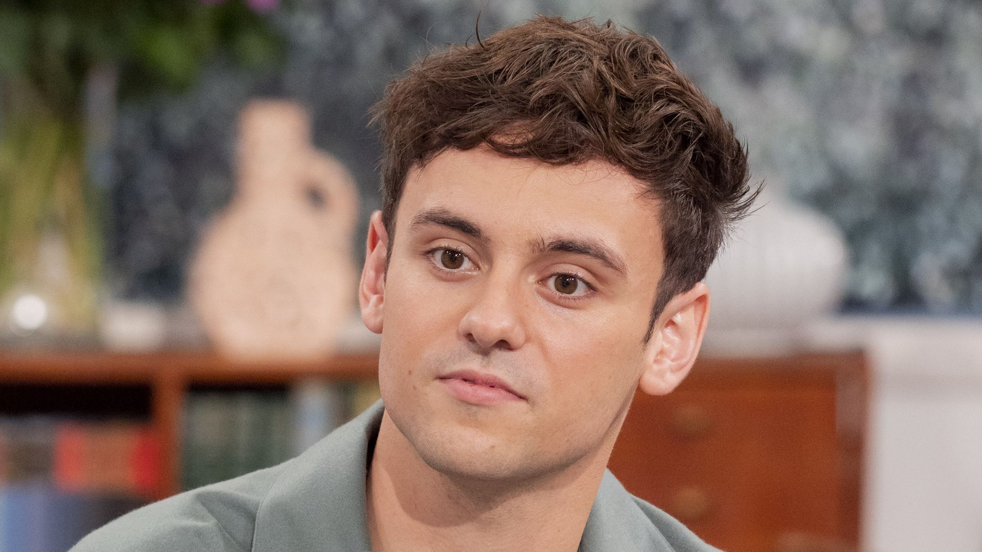 Tom Daley with a blank expression on a sofa