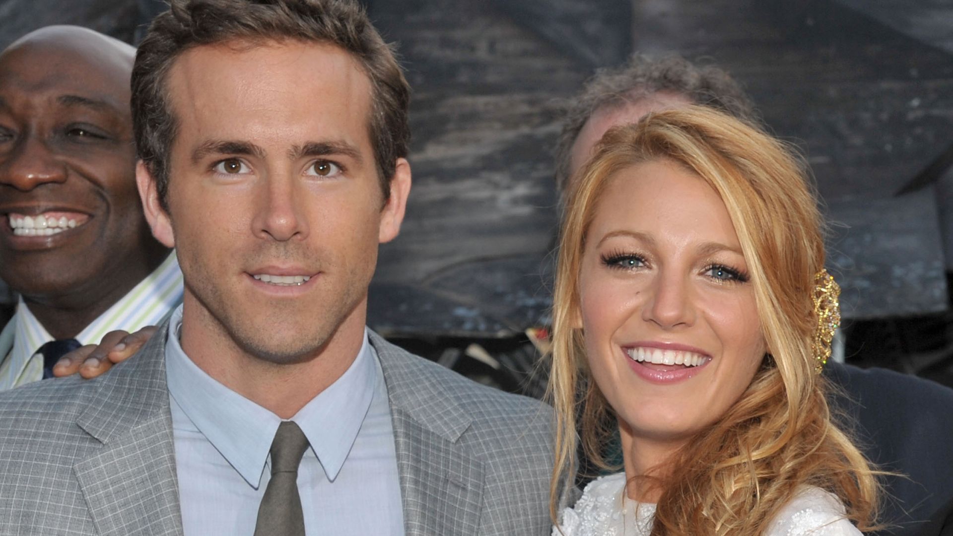 Blake Lively in a white dress with Ryan Reynolds in a grey suit smiling for photos at the Green Lantern premiere in 2011 