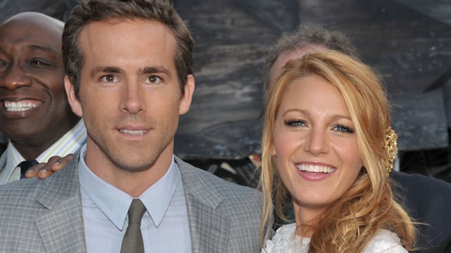 Blake Lively in a white dress with Ryan Reynolds in a grey suit smiling for photos at the Green Lantern premiere in 2011 