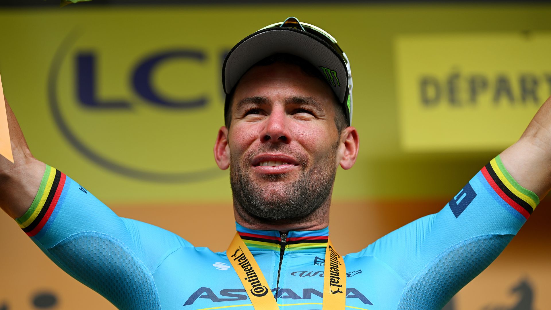 Mark Cavendish in a blue lycra outfit on a yellow podium