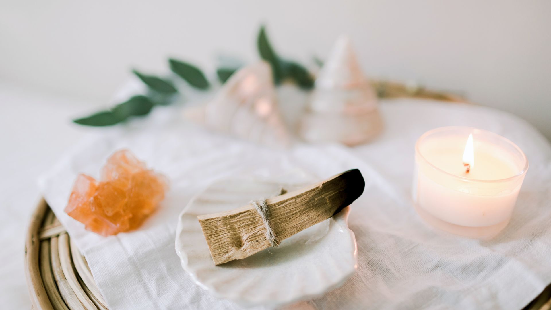 A wooden tray with ceramic plate on a linen cloth, eucalyptus leaves, candle, sea shells  and Palo Santo ready to burn. Ritual objects for spiritual practice. Ceremony with Palo Santo. Mental health.