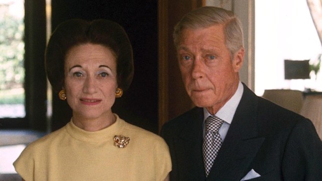 Wallis Simpson stands beside Edward, Duke of Windsor in 1966, in their ornately decorated Paris home. She wears a yellow dress and brooch; he’s in a dark suit with a polka-dot tie.