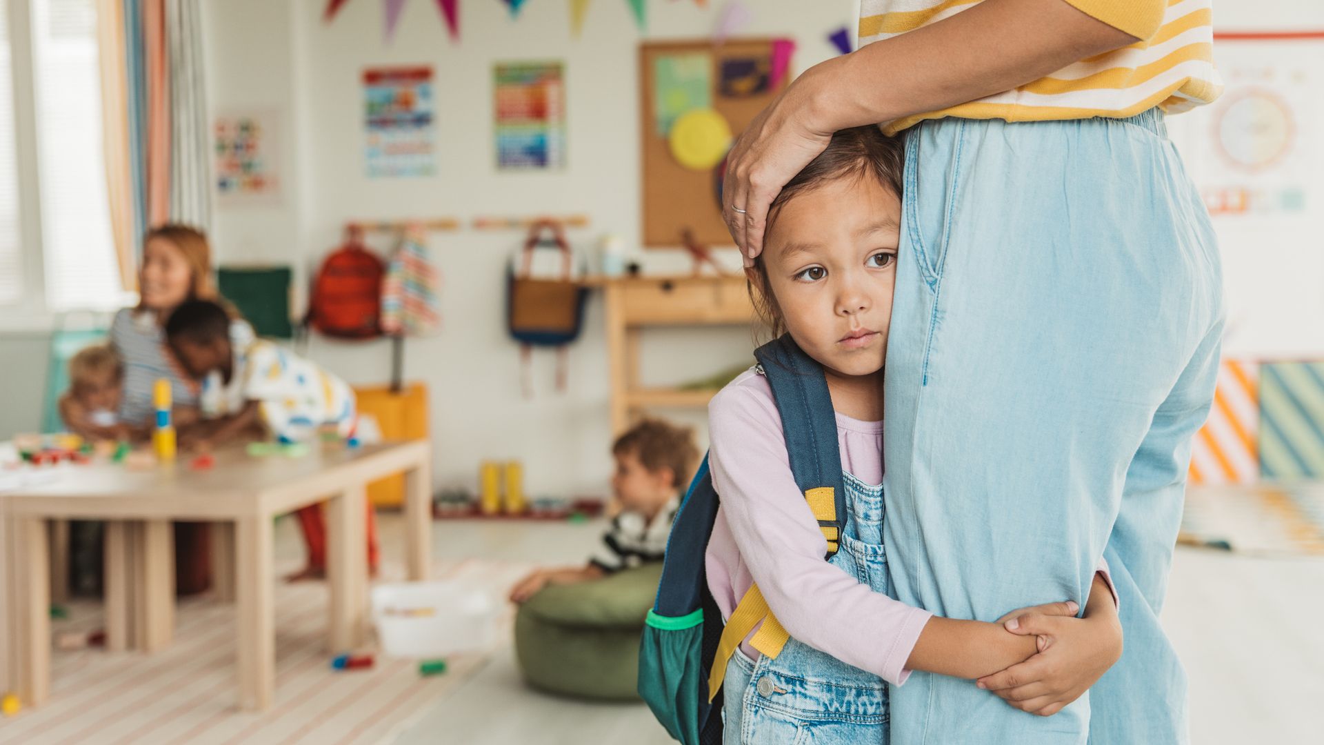 Preschool teacher in kindergarten classroom greeting new student, helping to easily assimilate with others.