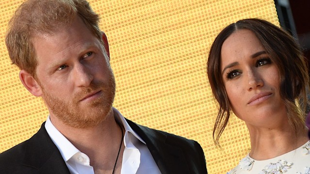 Prince Harry in a suit looking serious with Meghan Markle in a white dress