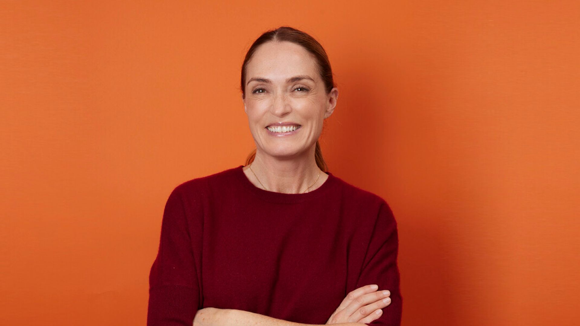 Woman in burgundy smiling on an orange background