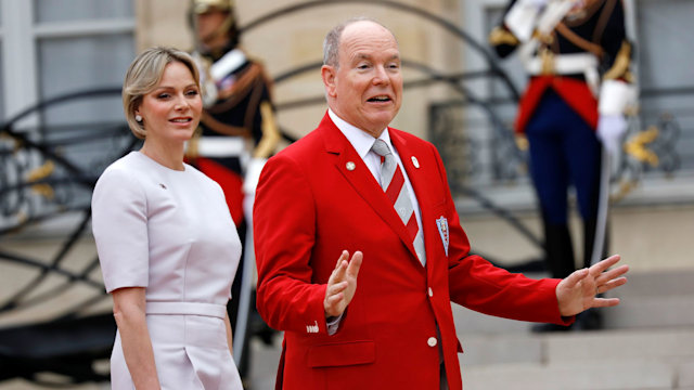 Princess Charlene in a white dress and Prince Albert in a red jacket