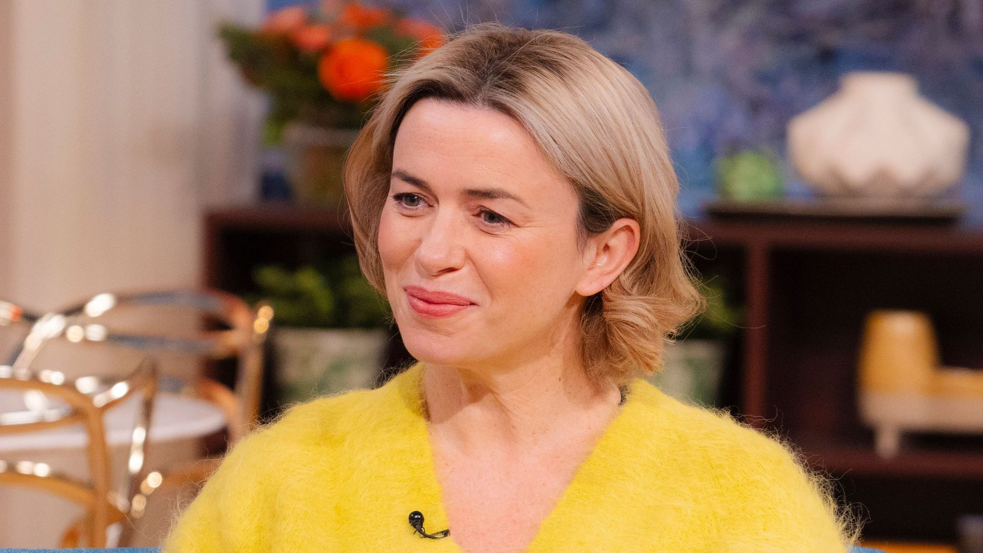 woman in yellow jumper sitting on blue sofa in tv studio