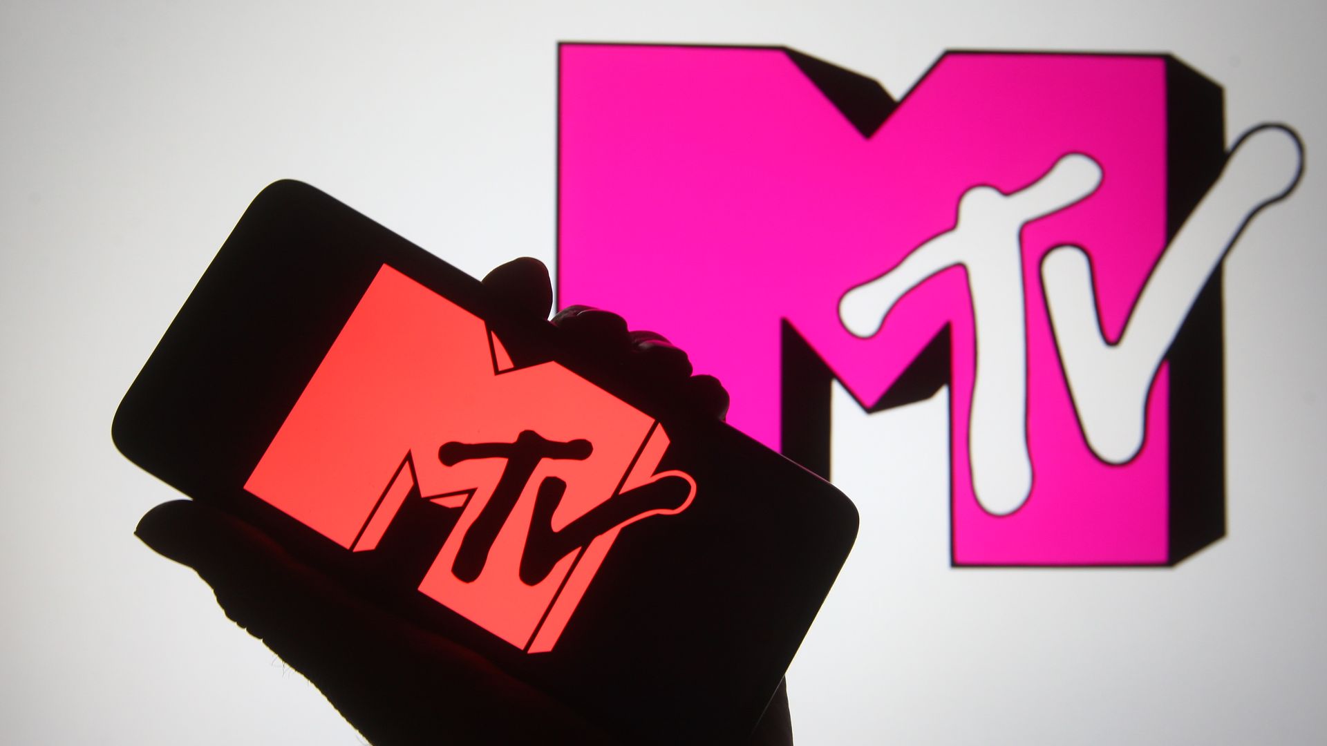 In this photo illustration a silhouette hand is seen holding a smartphone with MTV channel logo on a its screen.