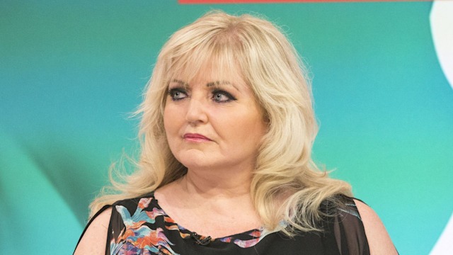 Linda Nolan sitting in a black floral dress