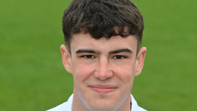 Josh Baker on a cricket field in a white uniform