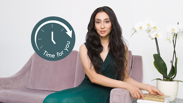 Young woman with long brown hair wearing a green dress sitting on a pink sofa