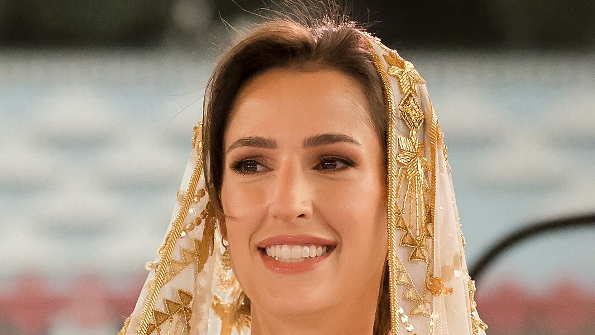 Princess Rajwa in gold and white outfit and headdress beside queen rania in pale blue dress
