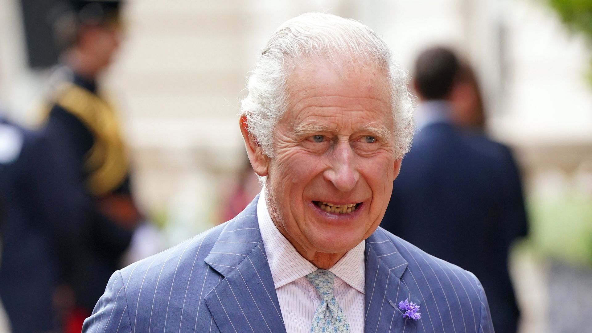 King Charles wears a pinstripe suit and carries a glass of Pimm's