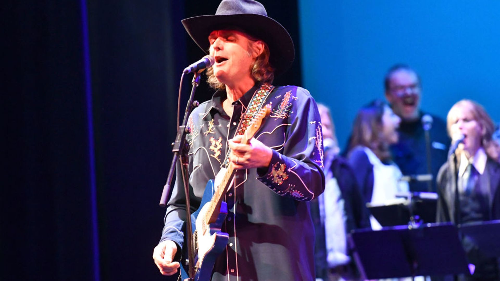 Val McCallum playing guitar on stage and singing into a microphone. 