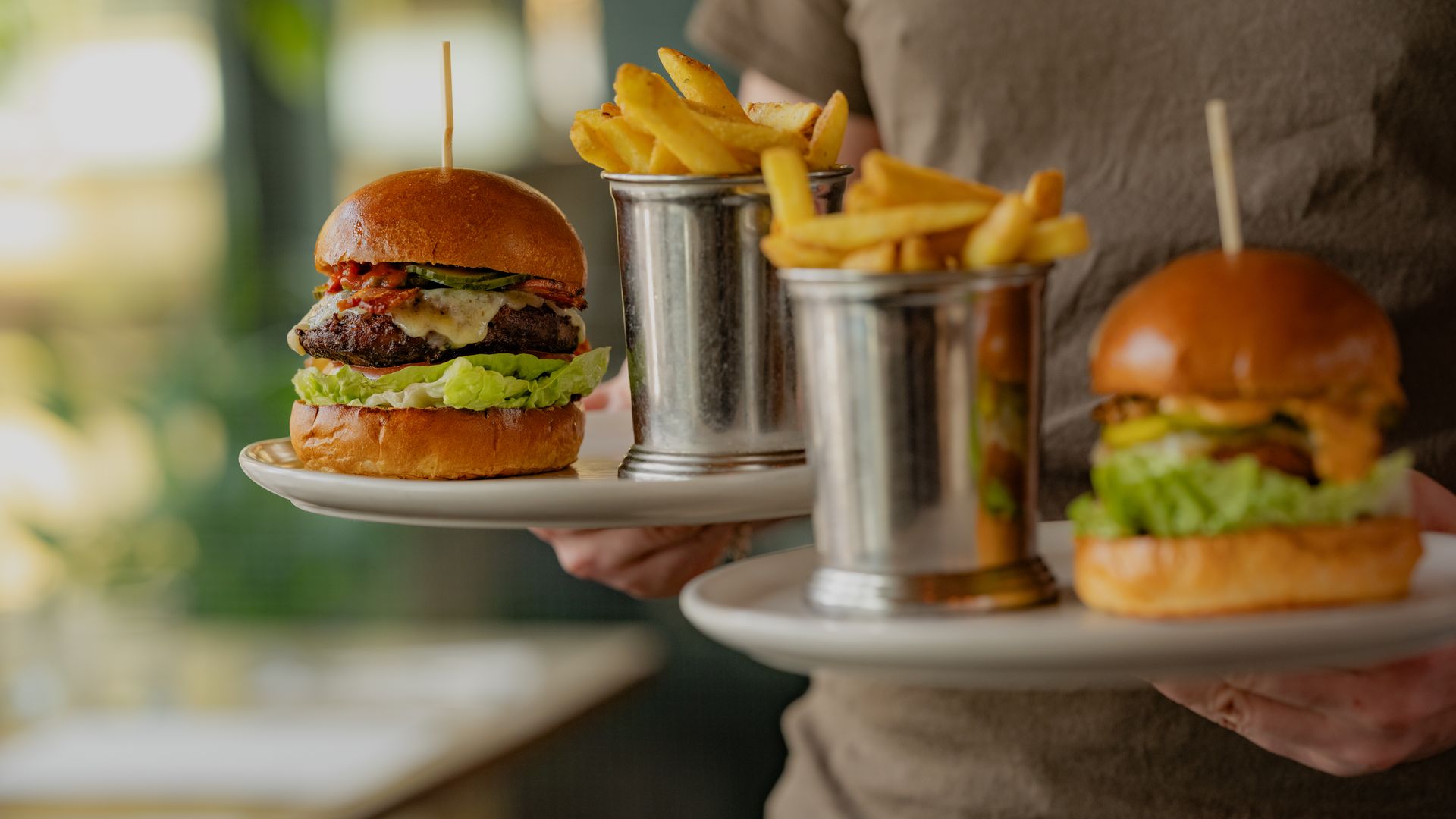A waiter in grey uniform delivering two burgers and two portions of chips