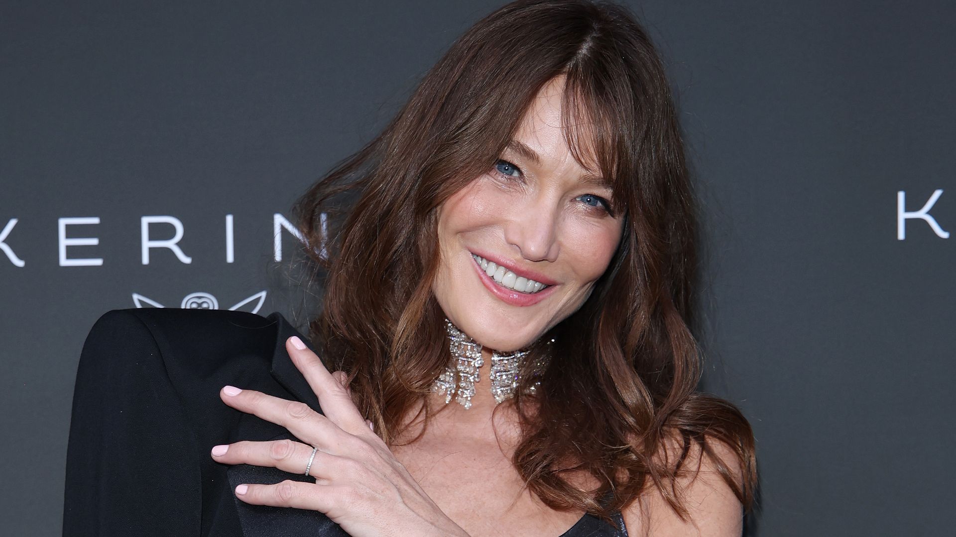 Carla Bruni posing for a photo in a black dress at a red carpet event