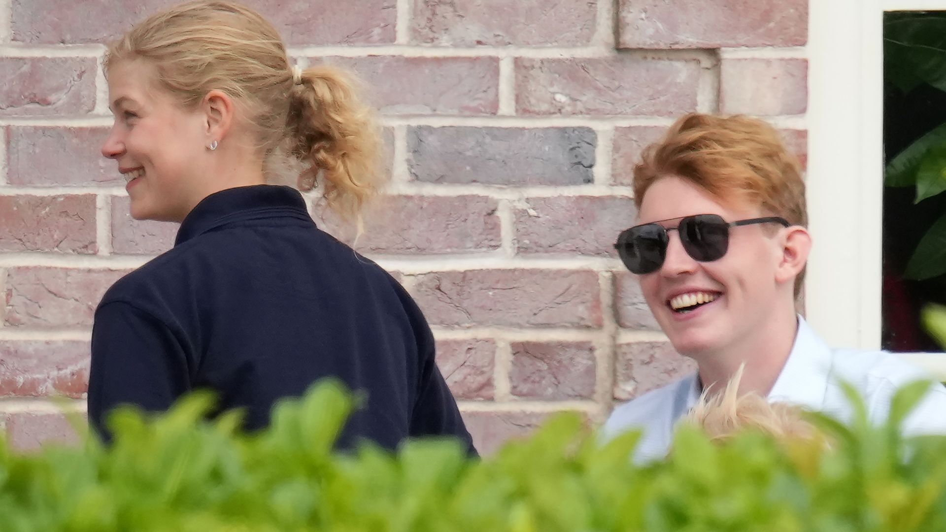 Lady Louise Windsor and Felix da Silva-Clamp smiling behind a hedge