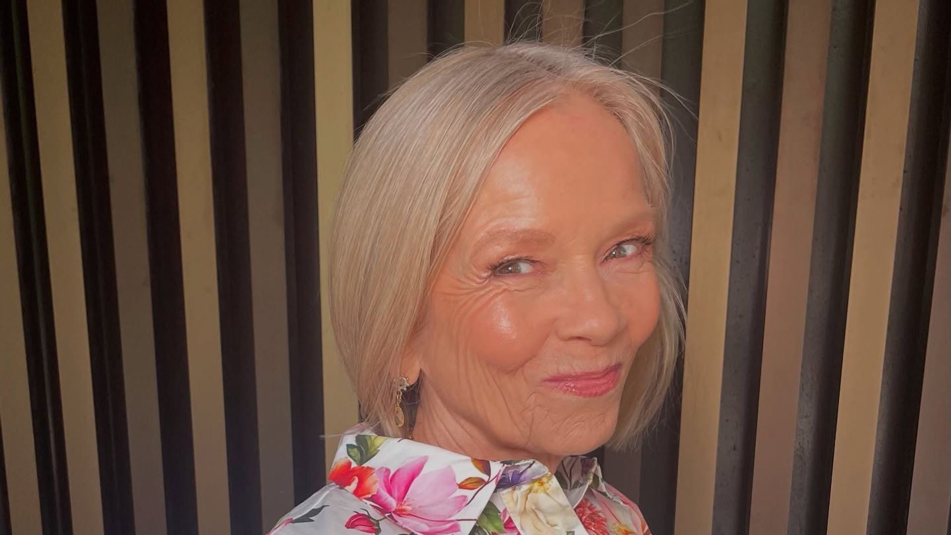 Older woman in floral dress smiling slightly with pink lipstick 