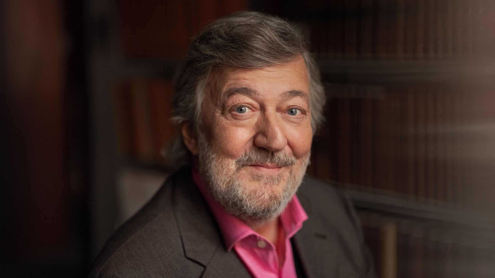 close up of man in brown blazer next to blurred book case