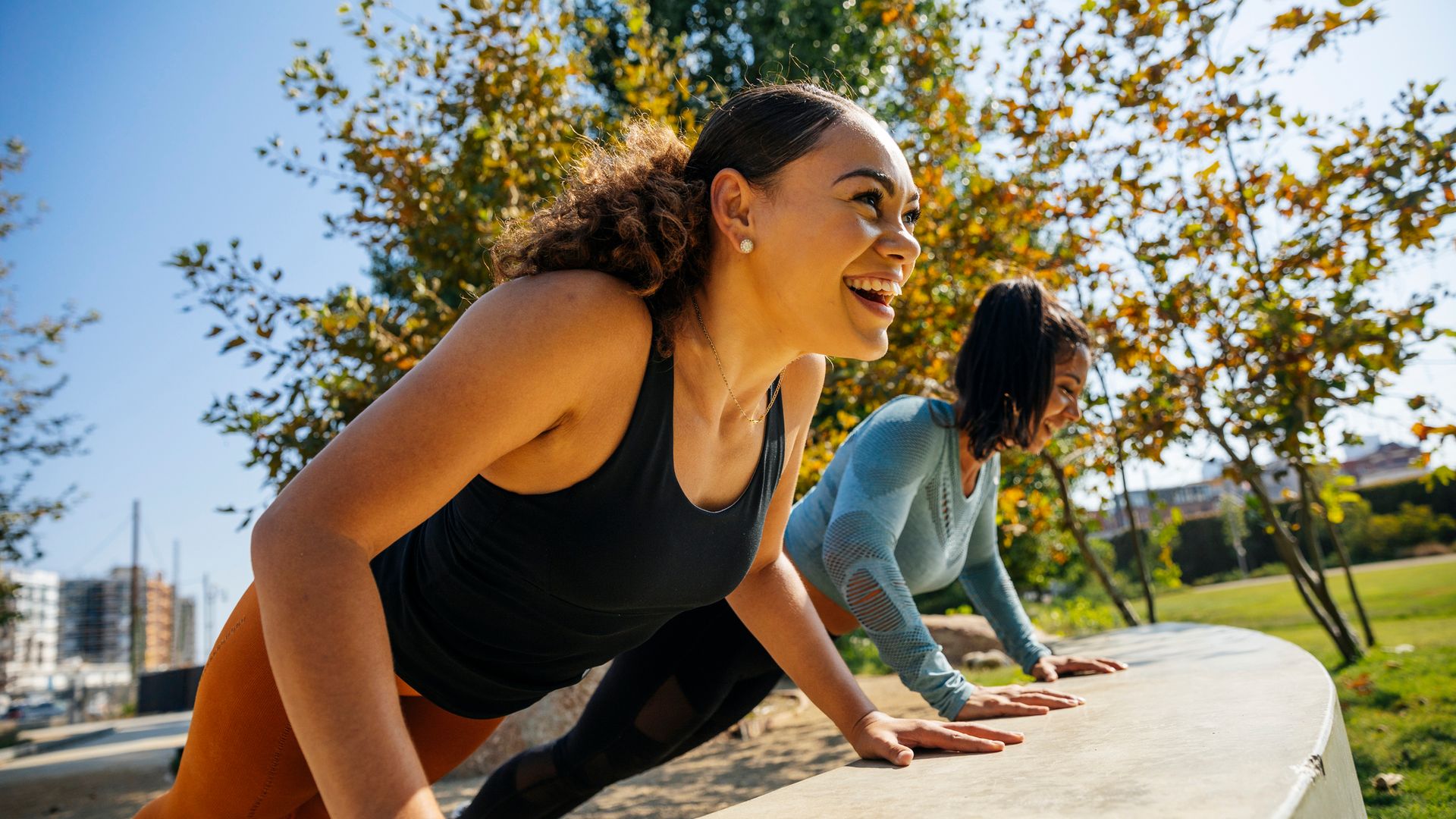 Cheerful women doing push-ups on retaining wall at park