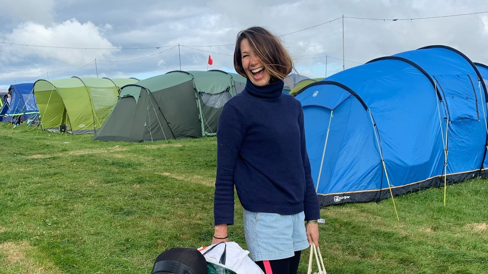 Rosie Green laughing while wheeling a suitcase along at a festival 