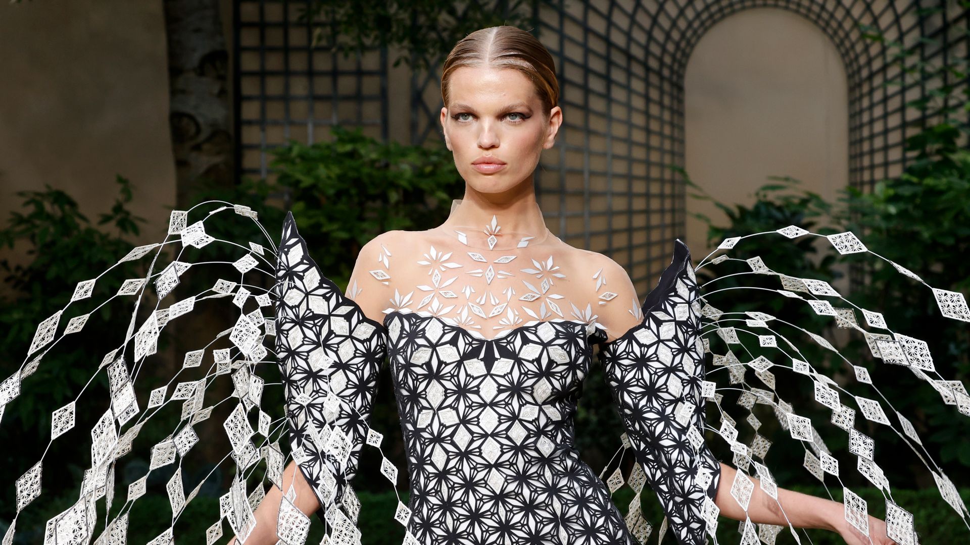 A model walks the runway in a patterned dress with diamond avant-garde detailing 