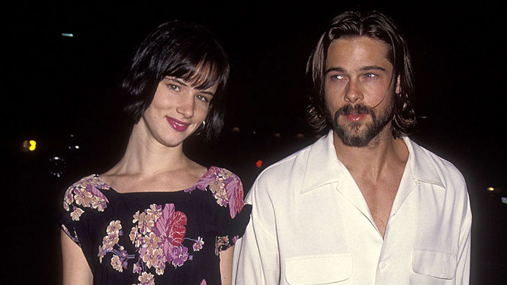 Juliette Lewis and Brad Pitt holding hands at the Johnny Suede Beverly Hills Premiere. She is wearing a floral dress while he is wearing a white shirt. 