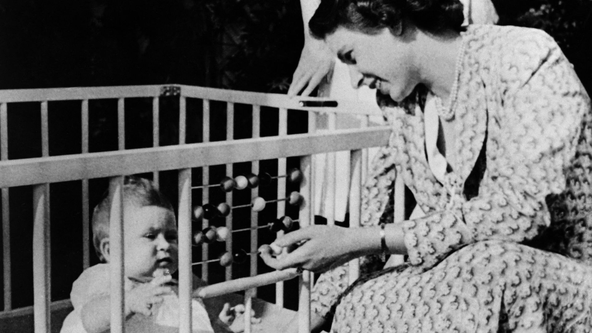 Queen Elizabeth II of England with her baby Charles in the crib