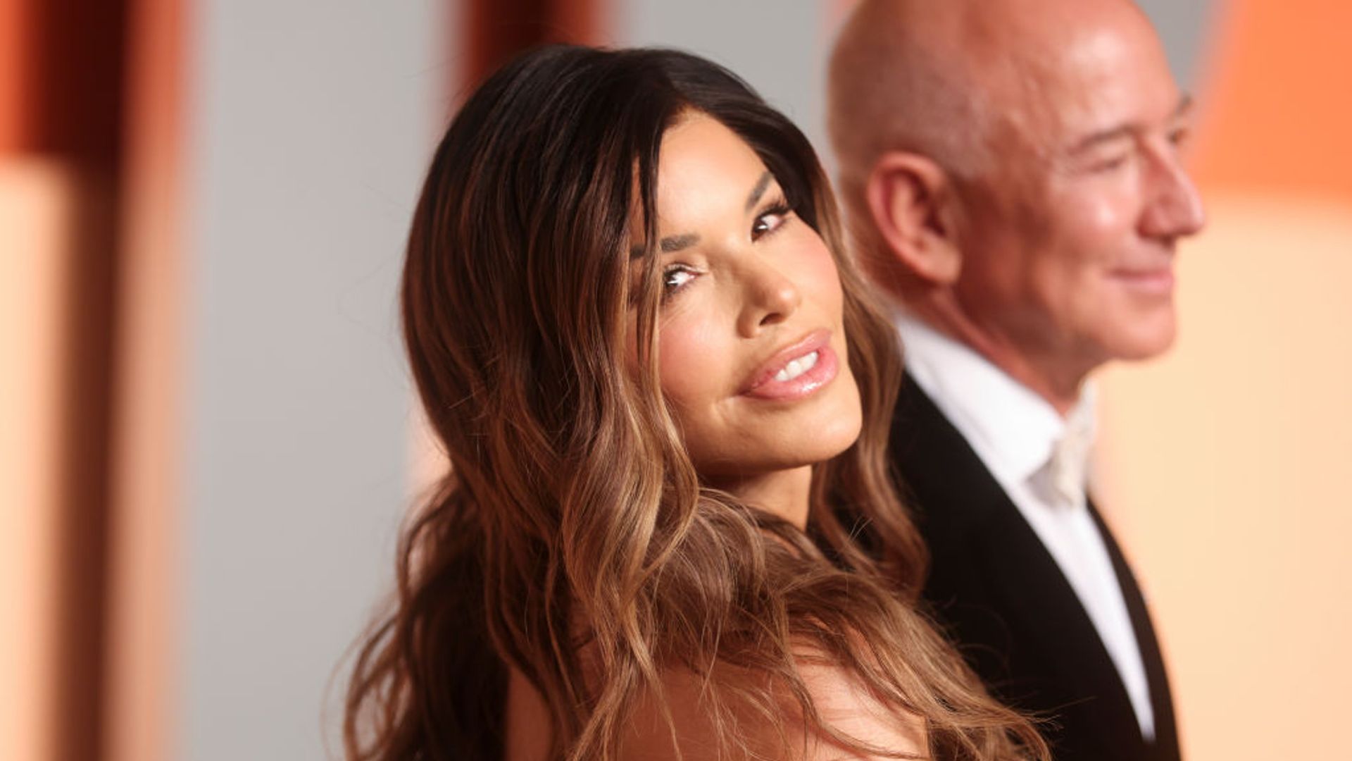 lauren sanchez looks into the camera with Jeff Bezos behind her 