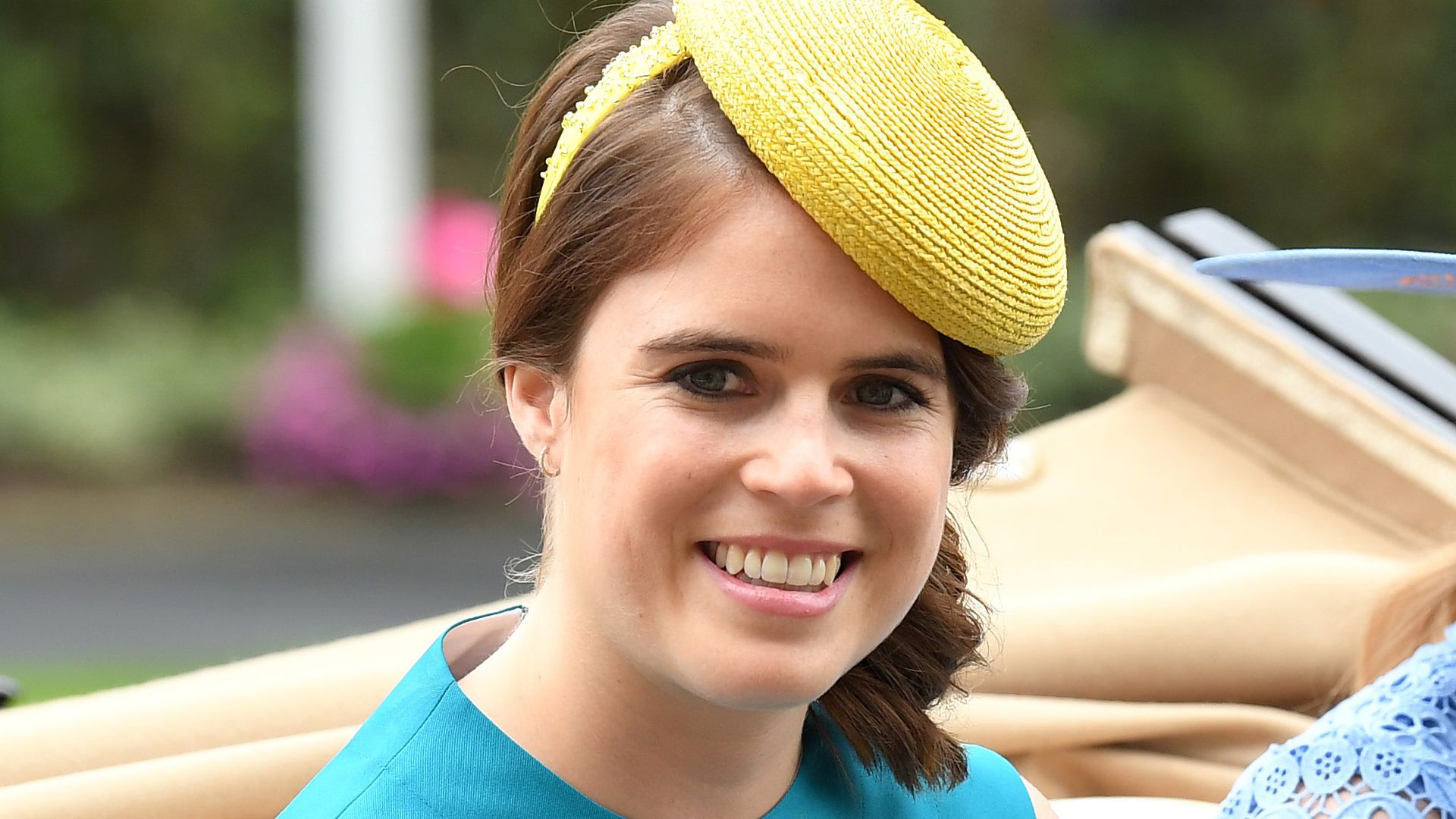 Princess Eugenie smiling and waving in a yellow hat
