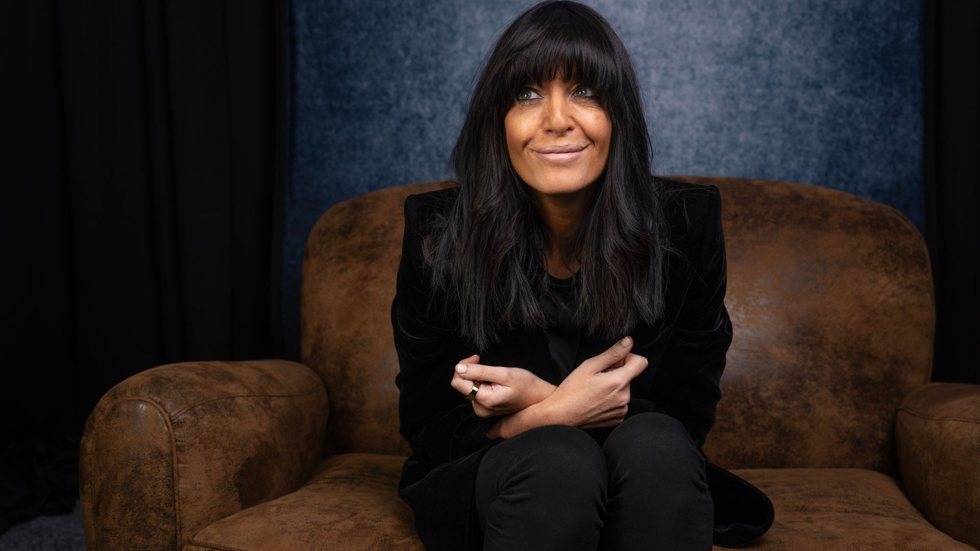 Claudia Winkleman in black on a a brown chair