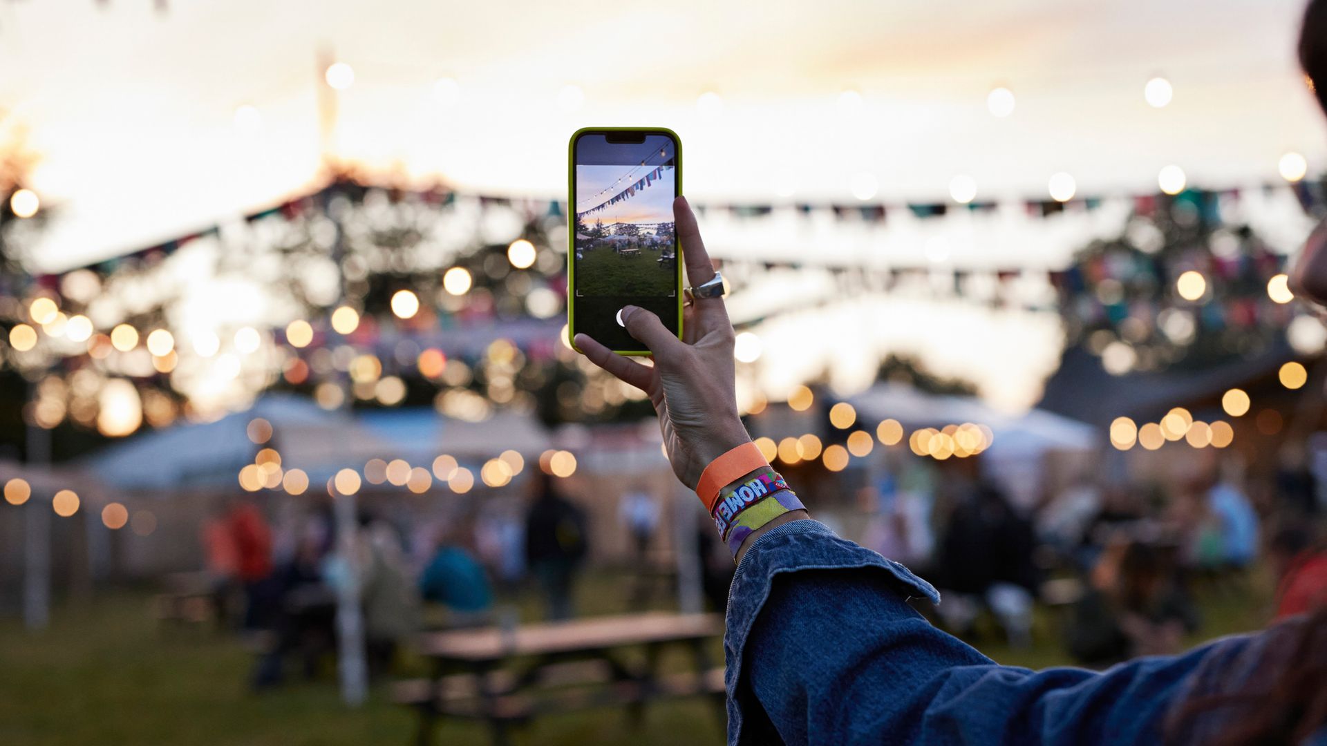 Hand of woman photographing bunting decoration through mobile phone at music festival