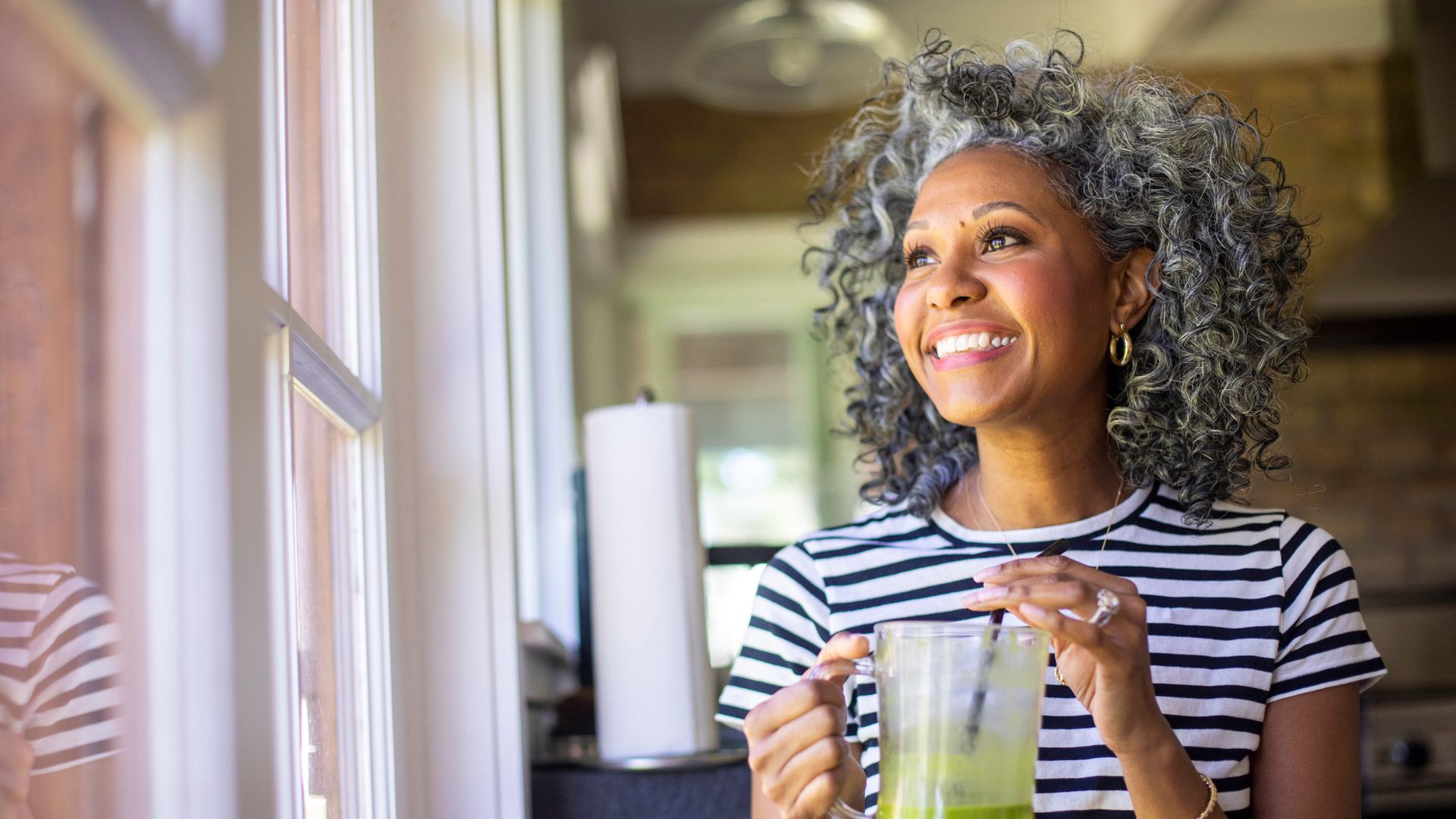 A beautiful black woman with white curly hair  drinks coffee in her kitchen