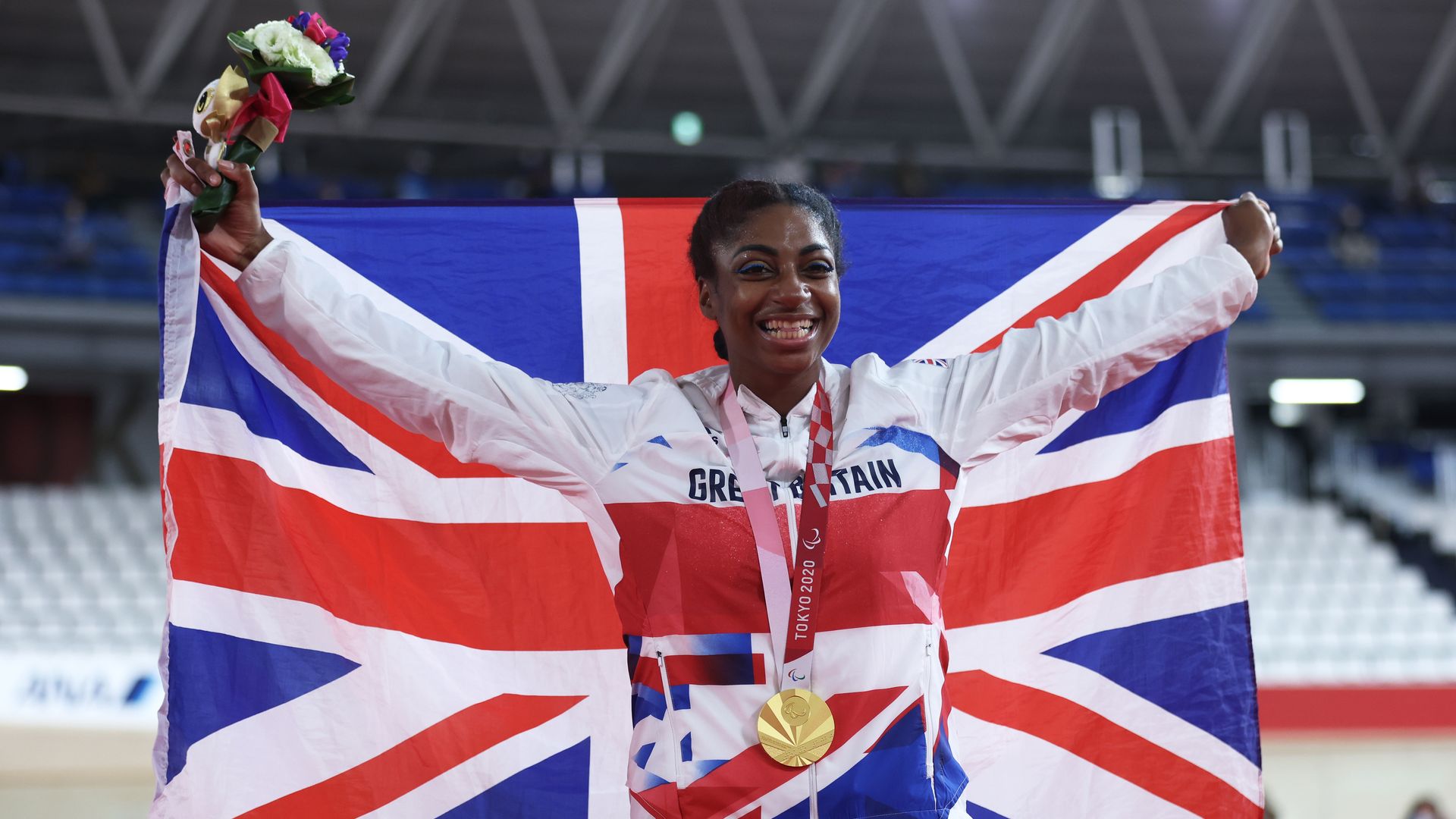 Kadeena Cox holding flowers with a British flag and gold medal