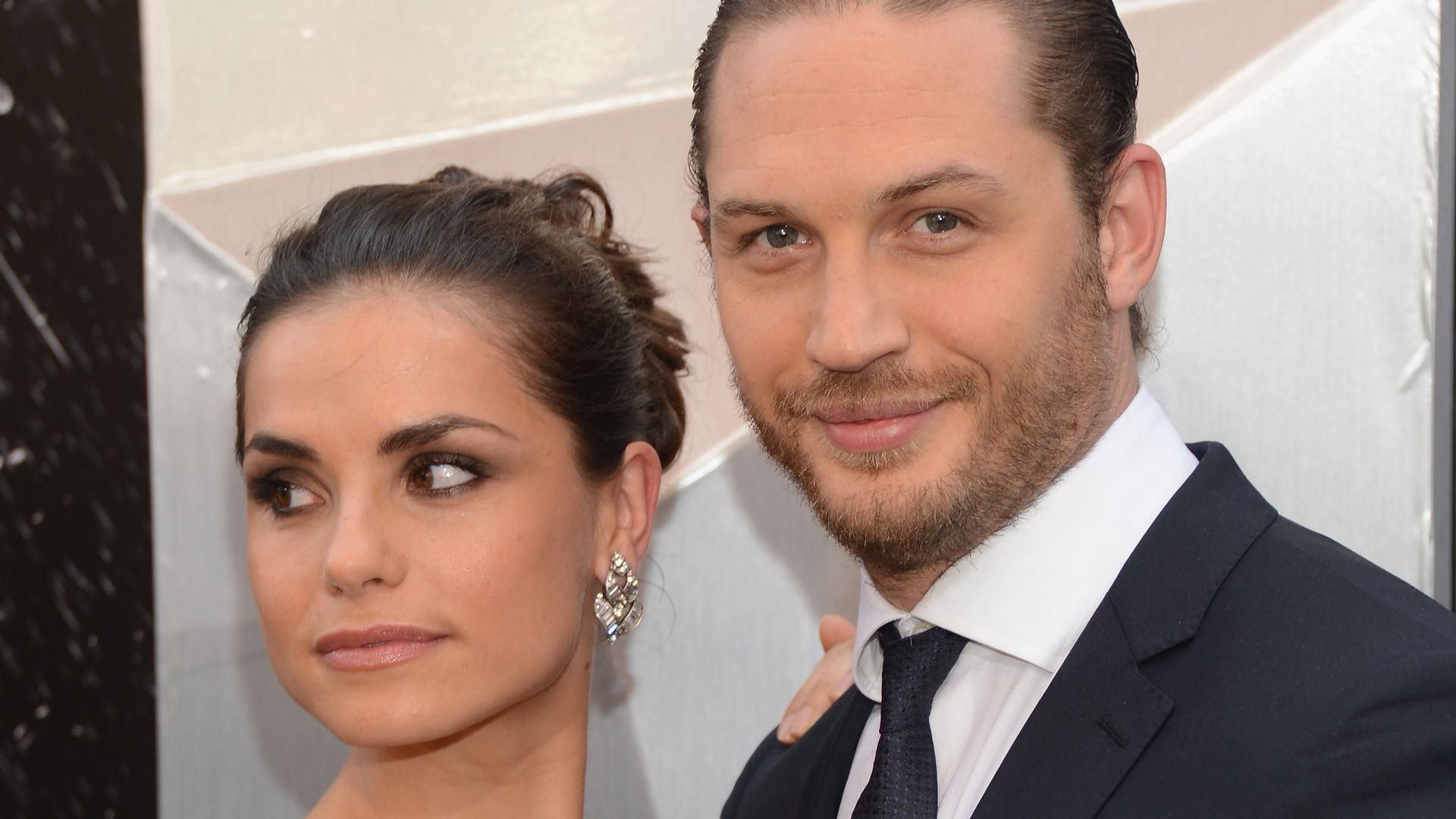 Tom Hardy in a suit with Charlotte Riley looking away in a strapless blue dress