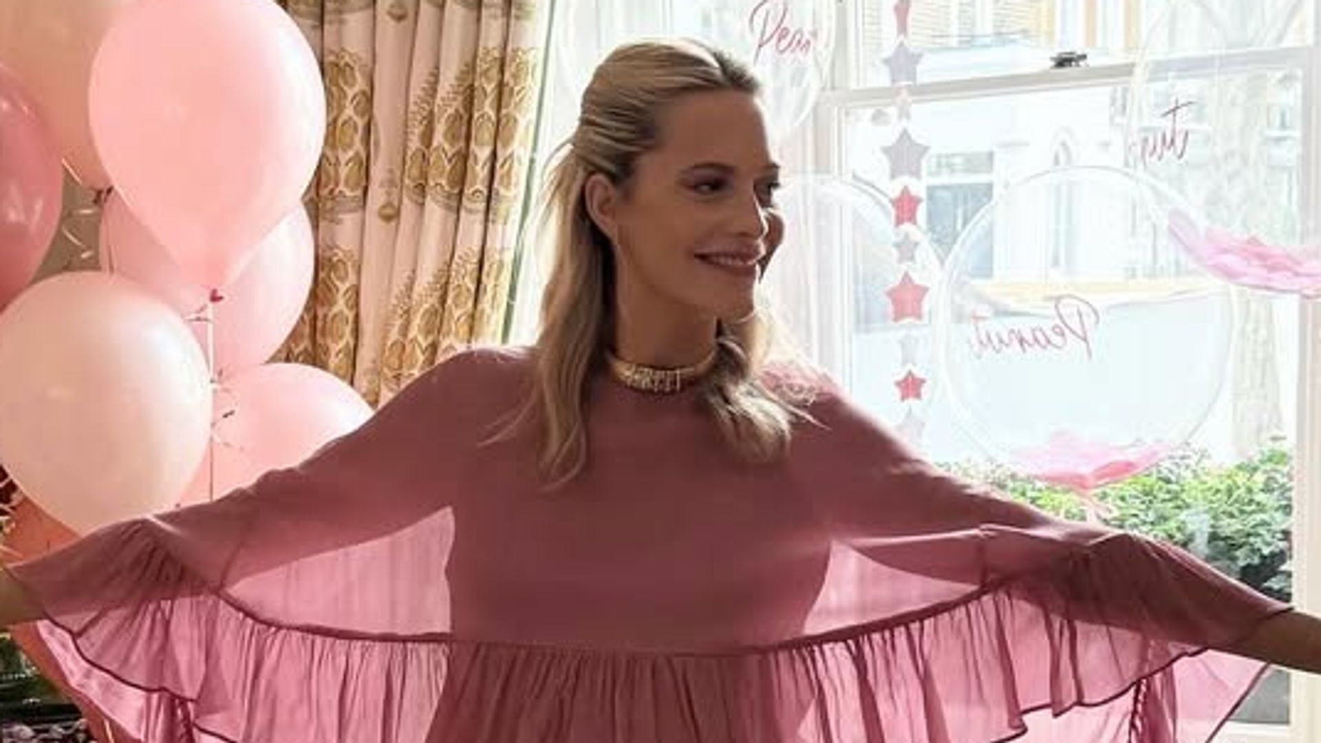Poppy Delevingne showcases the dramatic cape and ruffle detailing of her pink Monsoon dress, glowing with joy during her baby shower at home.
