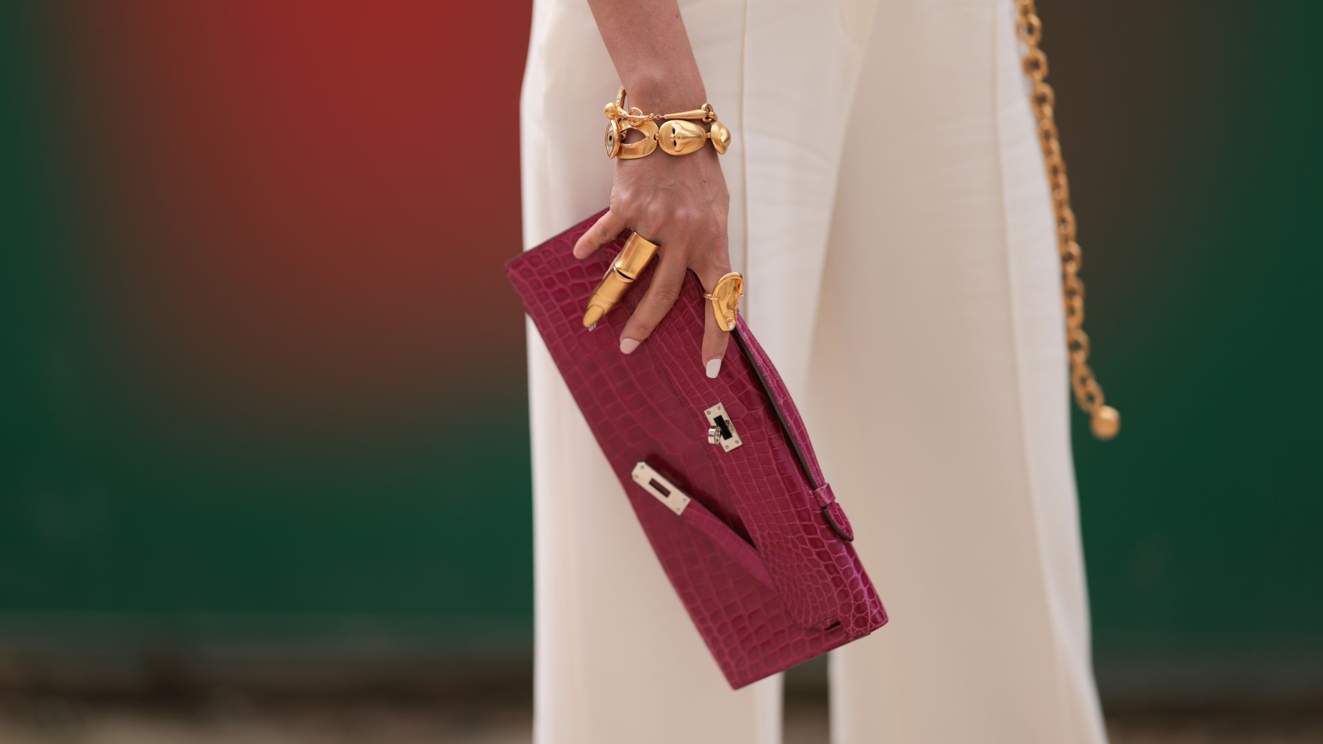 Woman wearing gold rings holding pink croc-effect clutch